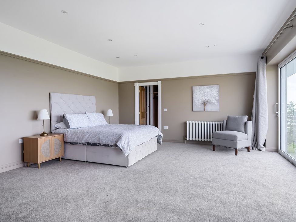 A bedroom with a bed chest of drawers armchair and sliding glass door at Plas Amherst in Harlech