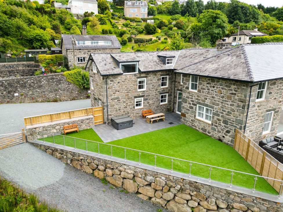 A stone house with a green lawn patio furniture and a hot tub at Plas Amherst in Harlech