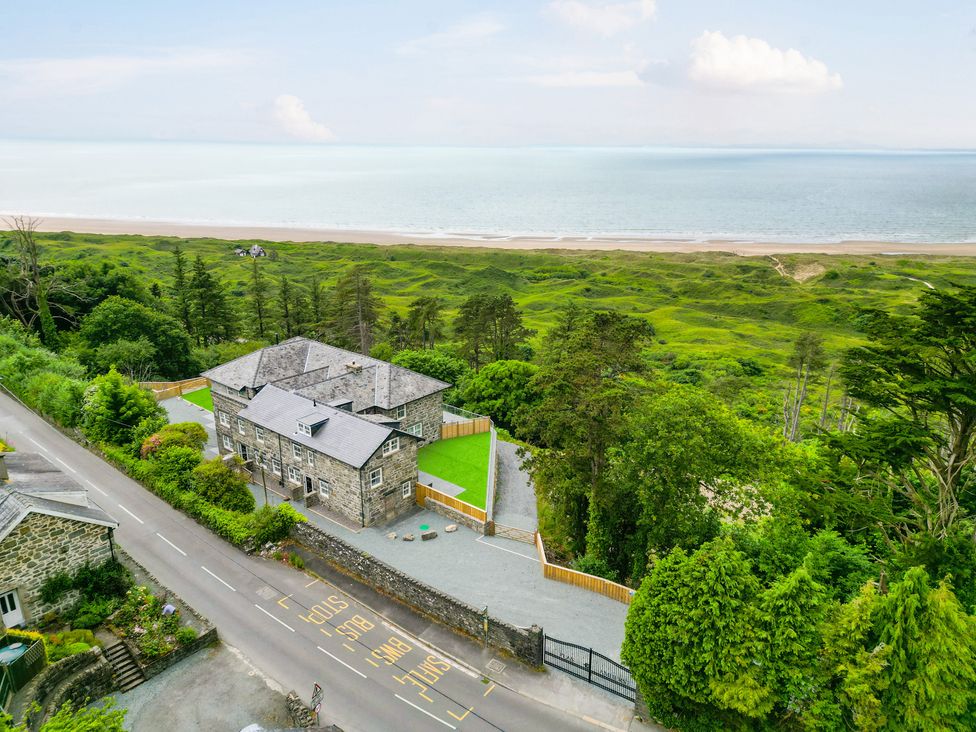A stone building near a road and green hills by the sea at Plas Amherst in Harlech