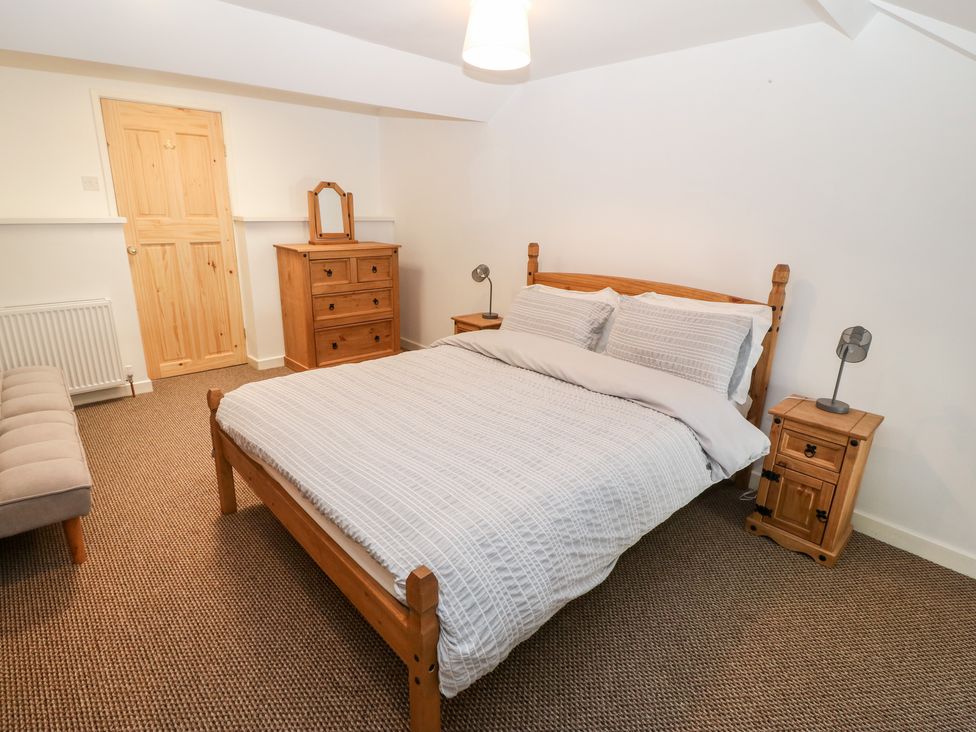 A bedroom with a wooden bed frame a chest of drawers and bedside tables with lamps at Weavers Cottage in Tremadog