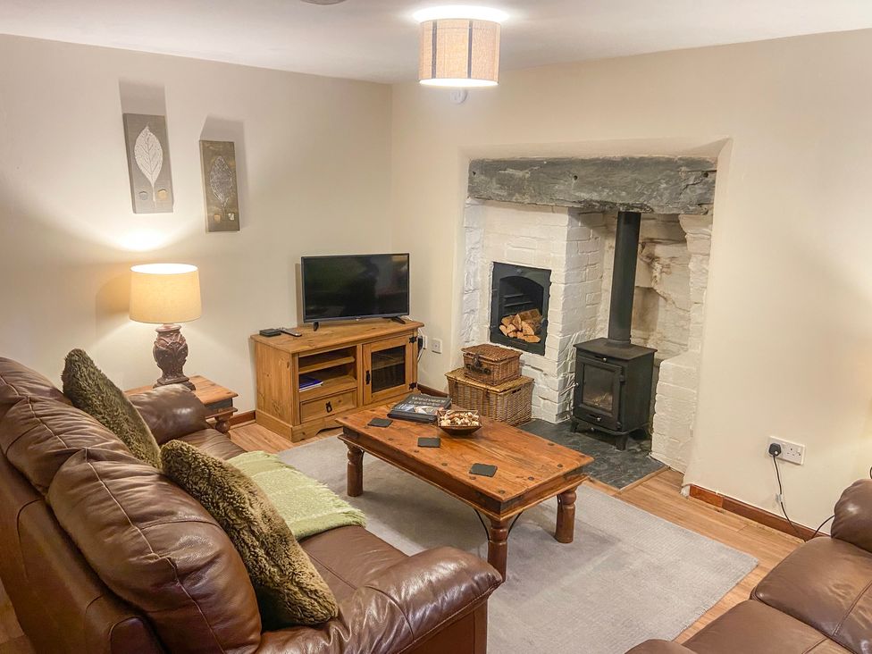 A living room with brown leather sofas a wooden coffee table a wood stove and a TV on a wooden stand at Weavers Cottage in Tremadog
