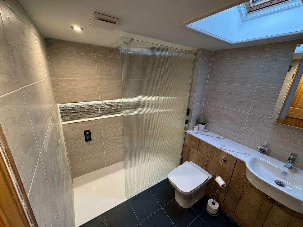 A bathroom with a walk in shower separated by a glass panel with a toilet and a sink with wooden cabinets underneath at Weavers Cottage in Tremadog