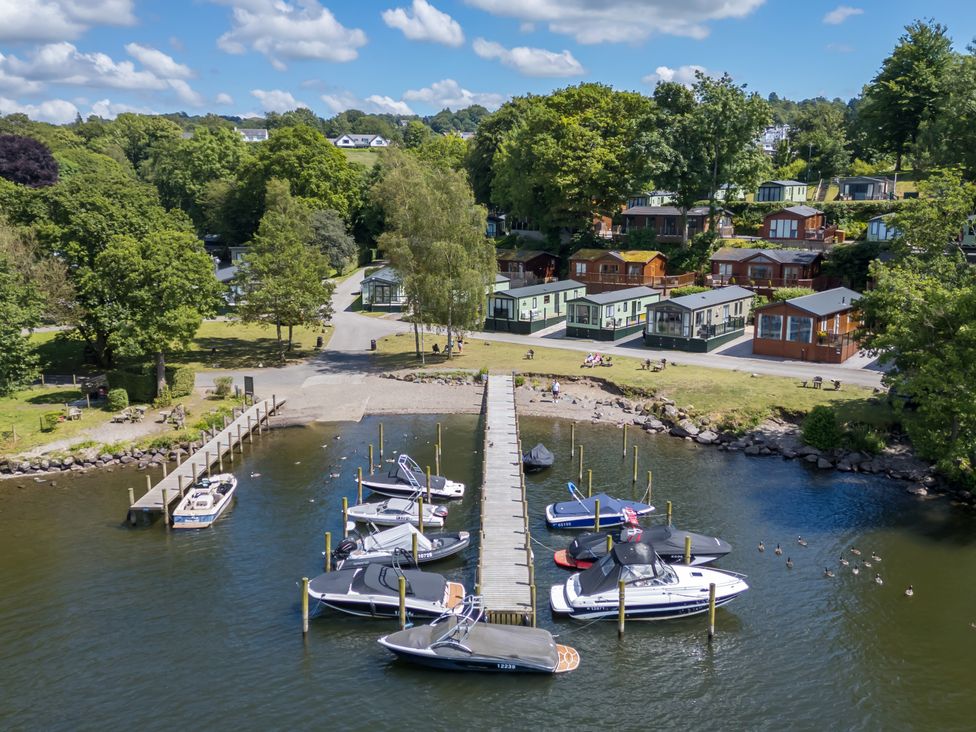 A lakeside scene with boats docked at a wooden pier and a row of holiday lodges behind at Daffodils Lodge Oakside 7 Fallbarrow Park in Bowness on Windermere