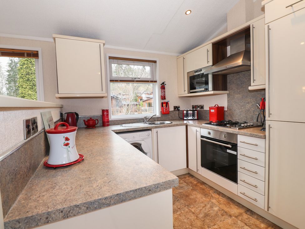 A kitchen with a countertop stove oven microwave washing machine and red kitchen accessories at Robins Nest Bowness 71 White Cross Bay near Windermere