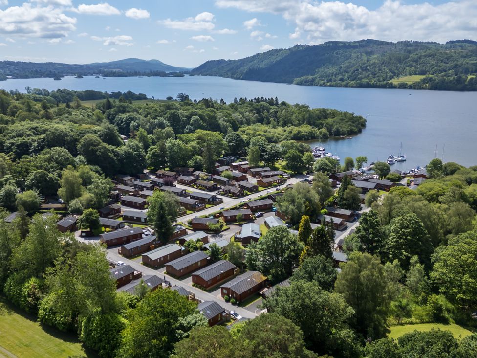 A residential area with multiple small houses surrounded by trees near a large body of water with hills in the background at Robins Nest in Bowness 71 White Cross Bay near Windermere
