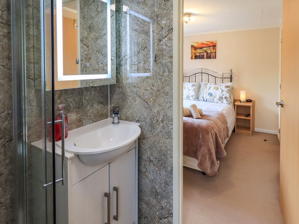 A bathroom with a sink and mirror next to a bedroom with a bed a bedside table and lamp at Robins Nest Bowness 71 White Cross Bay near Windermere