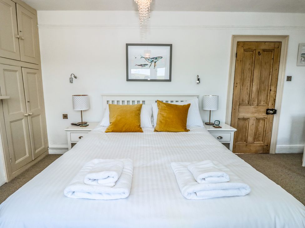 A bedroom with a white bed with two yellow pillows two folded towels bedside tables lamps a wooden door and built in cupboards at Seascape Dartmouth