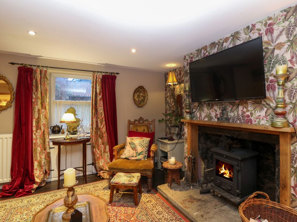 A living room with a wood burning stove television floral wallpaper and red curtains at Wonderland Cottage in Newburgh Fife