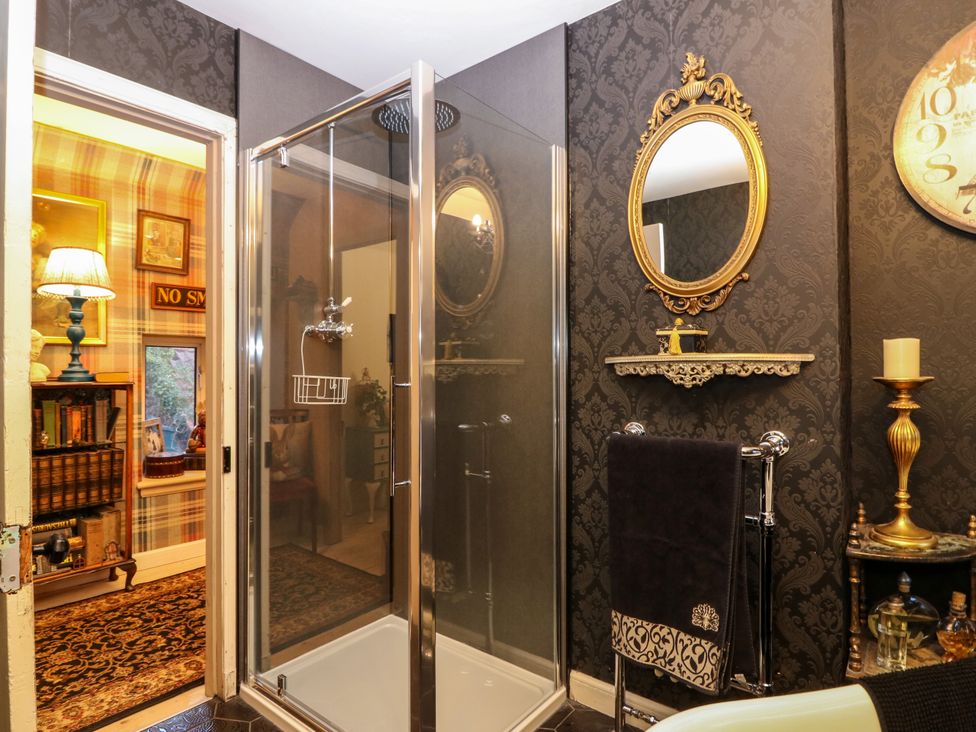 A bathroom with a glass shower enclosure a towel rack with a towel a gold framed mirror and a candle holder at Wonderland Cottage in Newburgh Fife