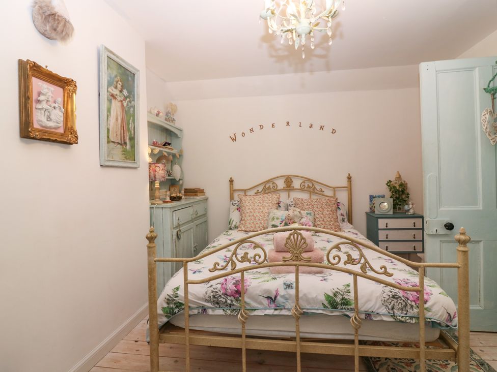 A bedroom with a metal bed frame floral bedding wooden cupboard and wall art at Wonderland Cottage in Newburgh Fife