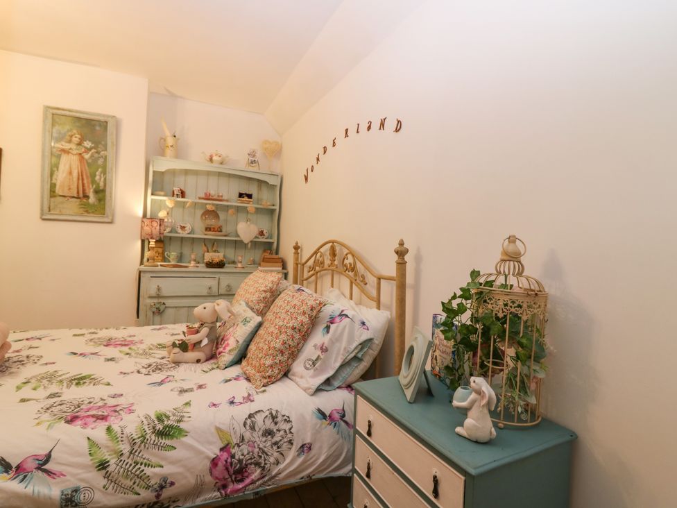 A bedroom with a bed floral bedding a light blue dresser with decorations and a shelf unit at Wonderland Cottage in Newburgh Fife
