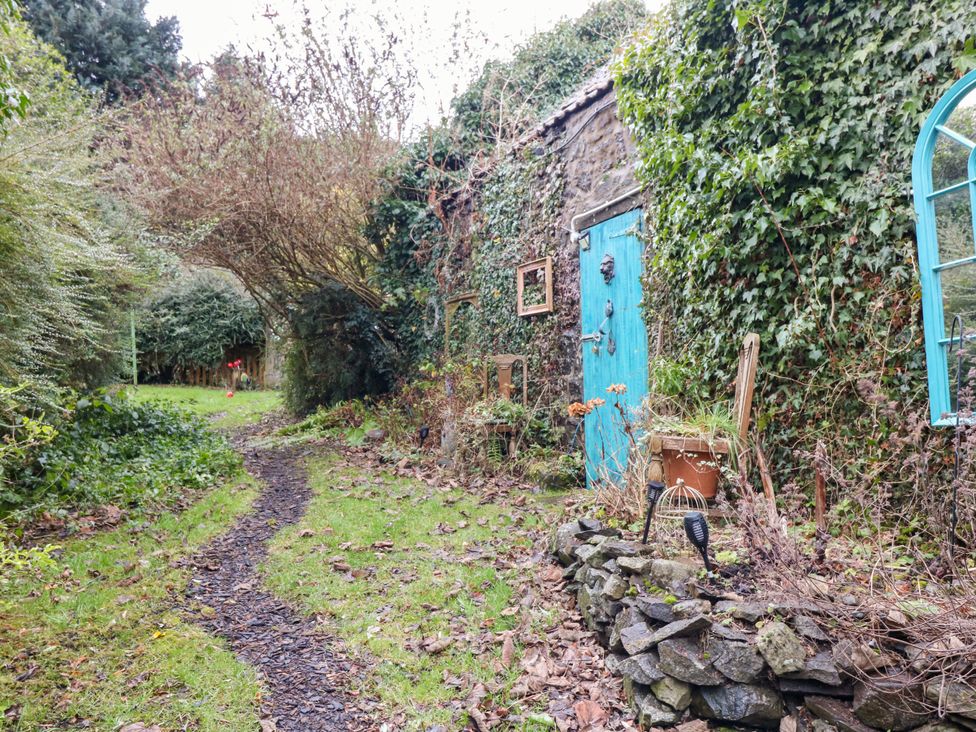 An outdoor garden path next to a stone wall covered with ivy and a blue door at Wonderland Cottage in Newburgh Fife