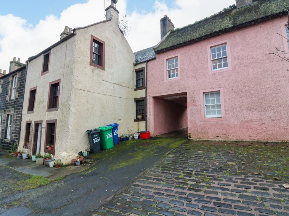 A cobblestone street with two attached houses and several trash bins outside at Wonderland Cottage in Newburgh Fife