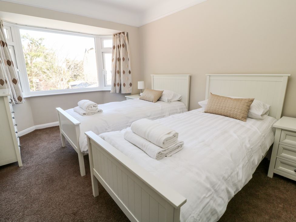 A bedroom with two single beds with folded towels on white bedding and a large window with patterned curtains at Harbour Lights in Torquay