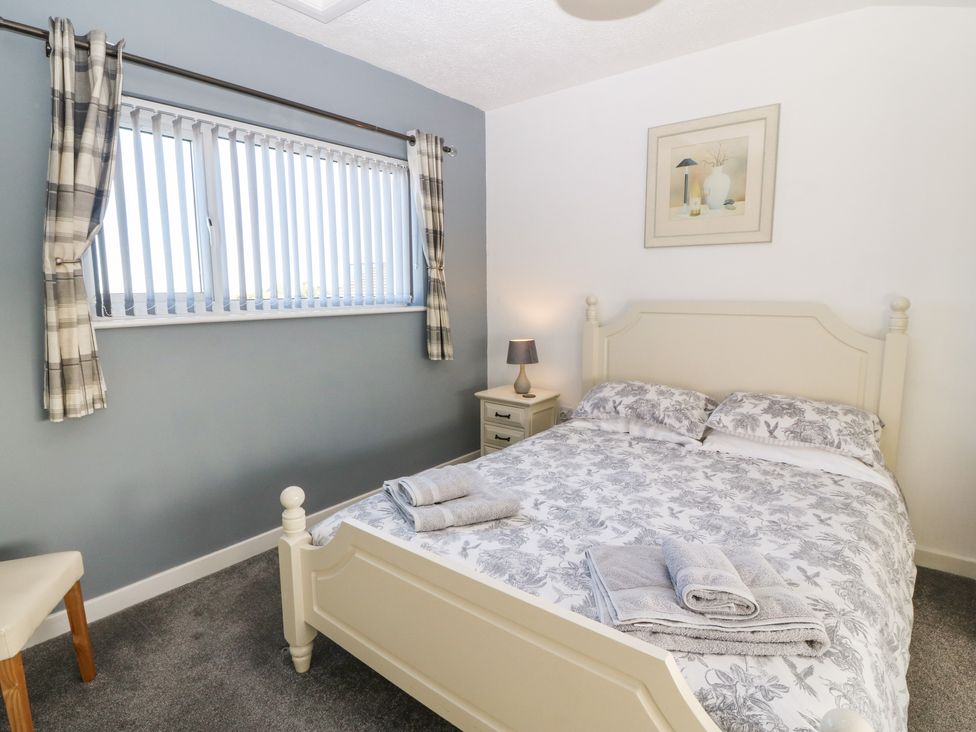 A bedroom with a bed with patterned bedding a nightstand with a lamp and a window with vertical blinds and curtains at Beach Reach in Valley