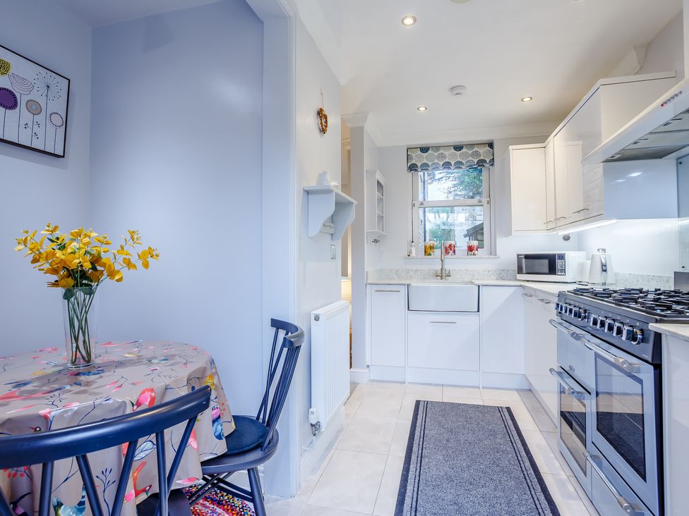 A kitchen with a dining table and chairs a sink stove microwave and window at Jasmine Cottage in Mickleton Gloucestershire
