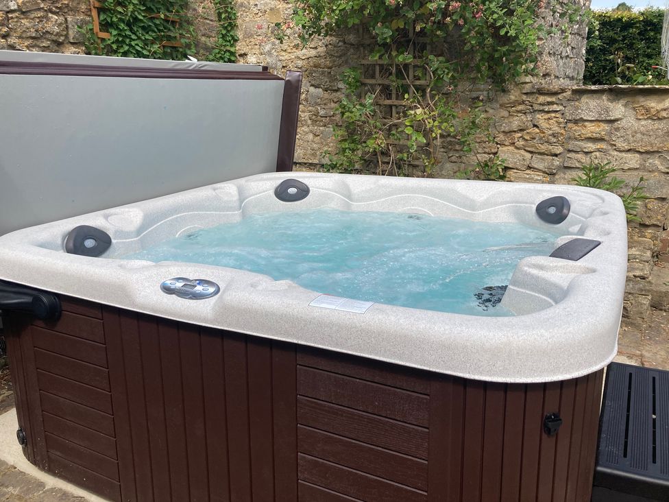 An outdoor hot tub filled with water against a stone wall with greenery at The Stable House in Sherborne