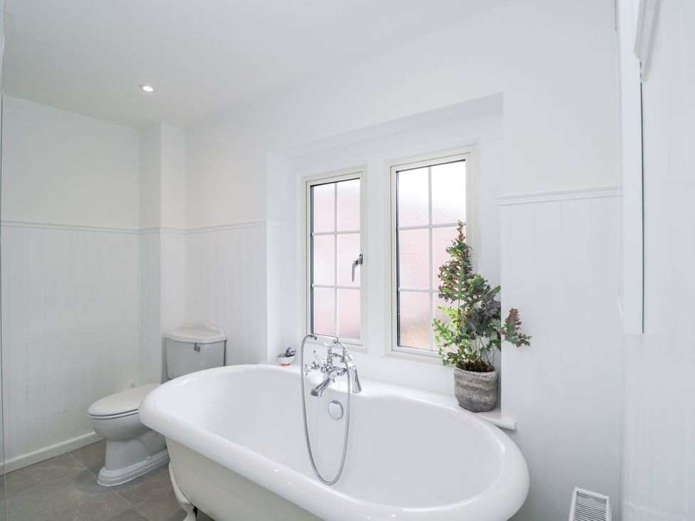 A bathroom with a white bathtub a toilet and two windows with a plant on the windowsill at The Stable House in Sherborne