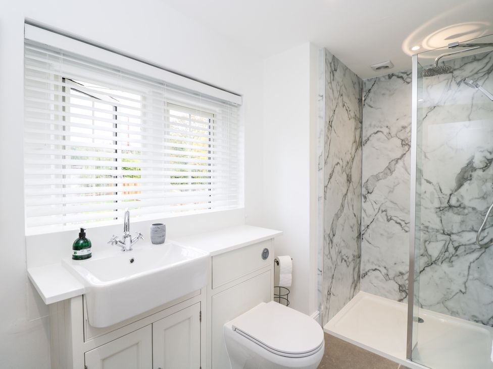 A bathroom with a white sink and cabinet toilet and a shower with marble walls at The Stable House in Sherborne