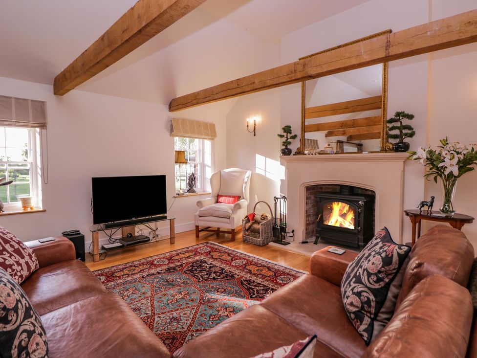 A living room with a leather sofa a patterned rug a fireplace and a television at Little Pontus in Molash near Challock