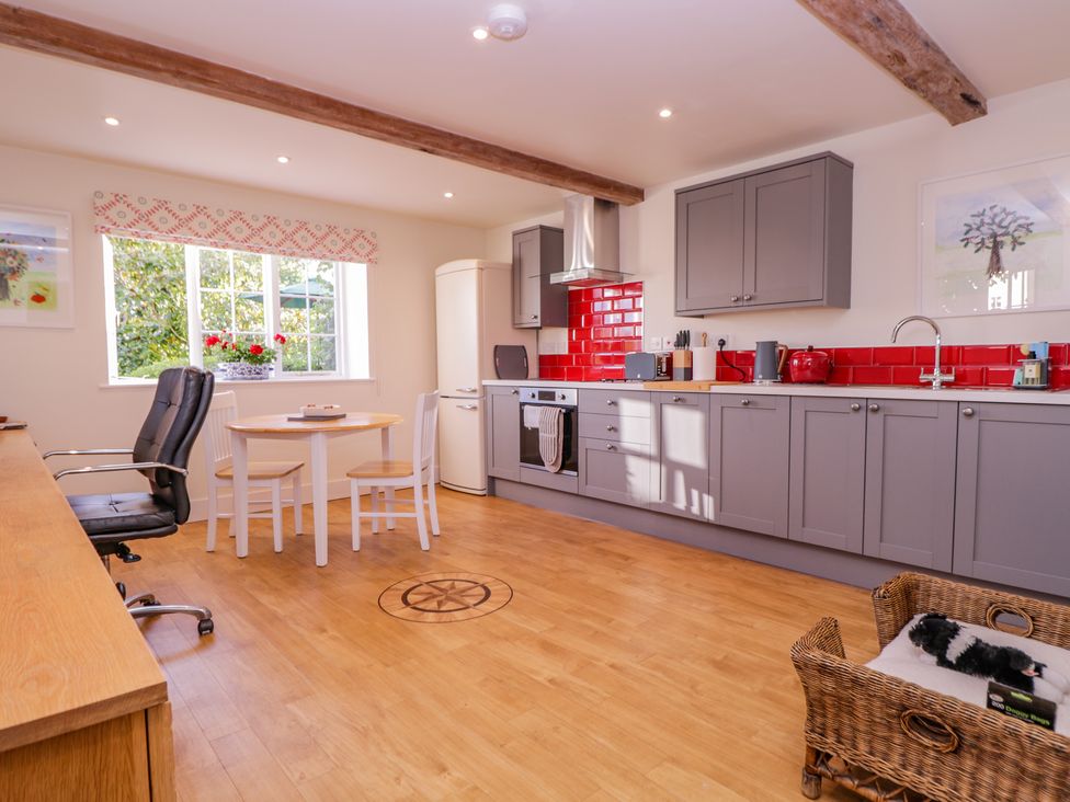 A kitchen with gray cabinets red backsplash a round table white chairs and a black office chair at Little Pontus in Molash near Challock