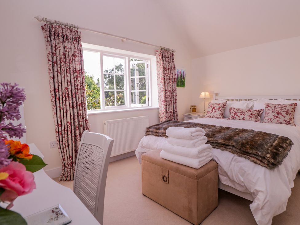 A bedroom with a bed with pillows and a fur throw a window with floral curtains and a chair by a desk at Little Pontus Molash near Challock