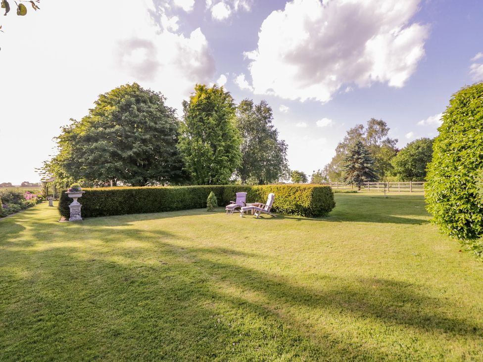 A garden with lawn chairs and hedges surrounded by trees under a partly cloudy sky at Little Pontus in Molash near Challock