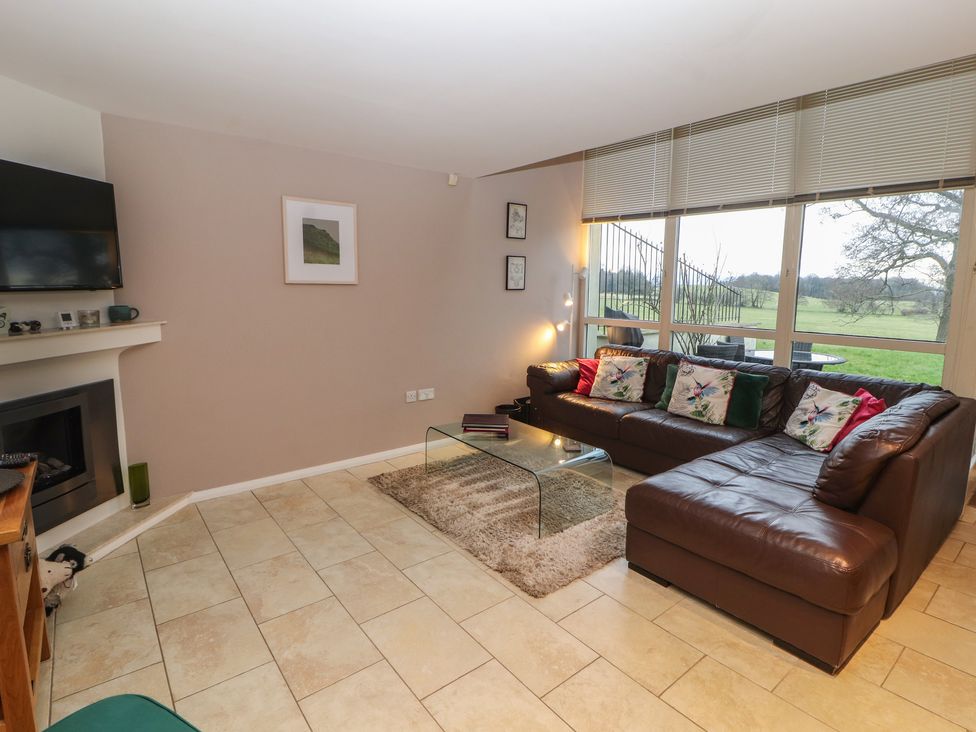 A living room with a brown leather sectional sofa and a glass coffee table on a rug at Lark Meadow in Kirkby Lonsdale