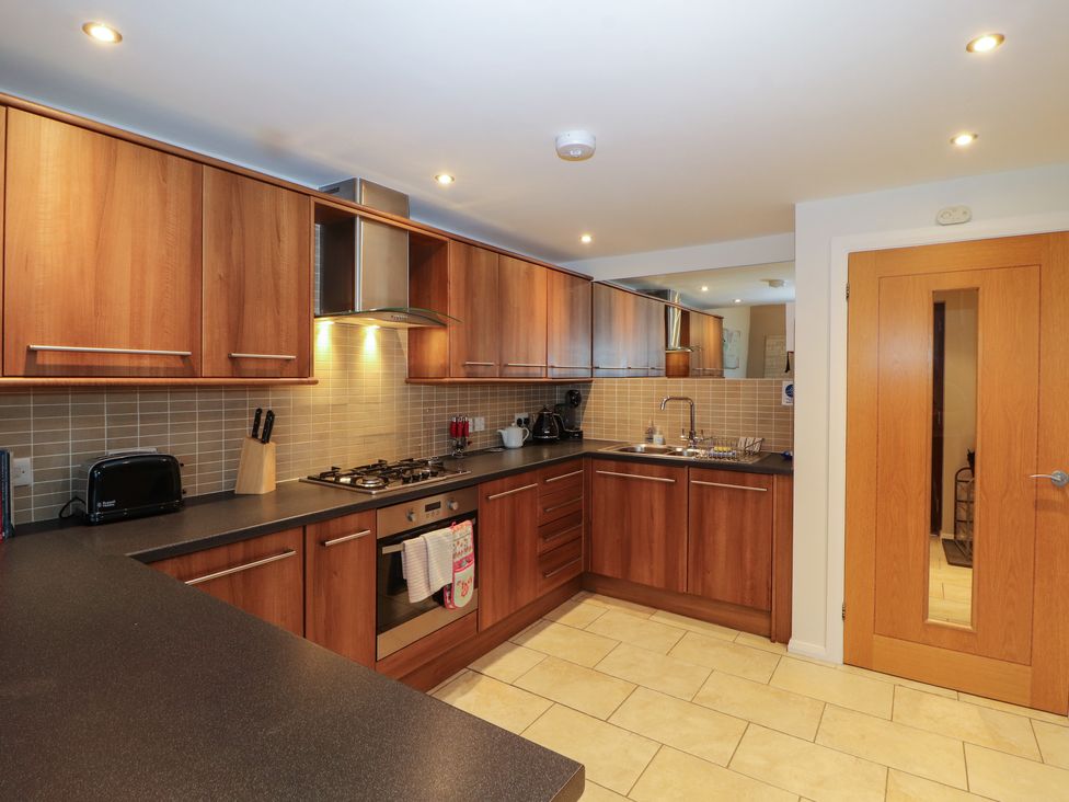 A kitchen with wooden cabinets black countertops tiled floor and a wooden door at Lark Meadow in Kirkby Lonsdale