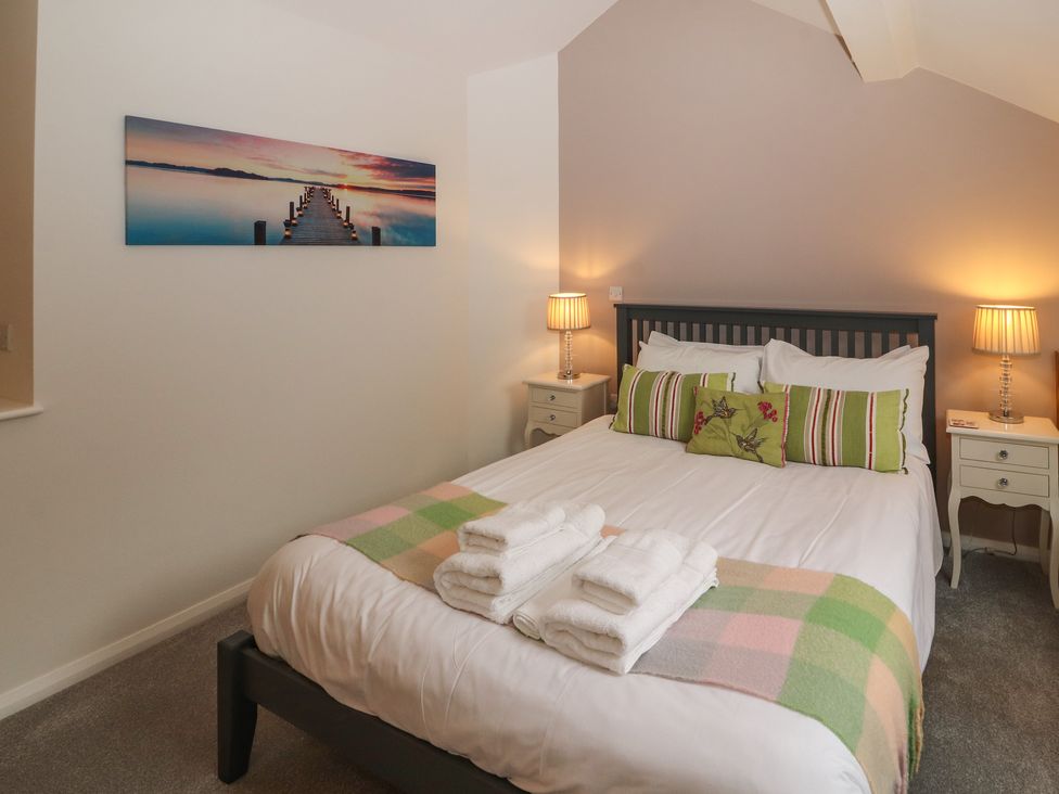 A bedroom with a bed with pillows and towels on it two bedside tables with lamps and a wall picture of a lake at Lark Meadow in Kirkby Lonsdale