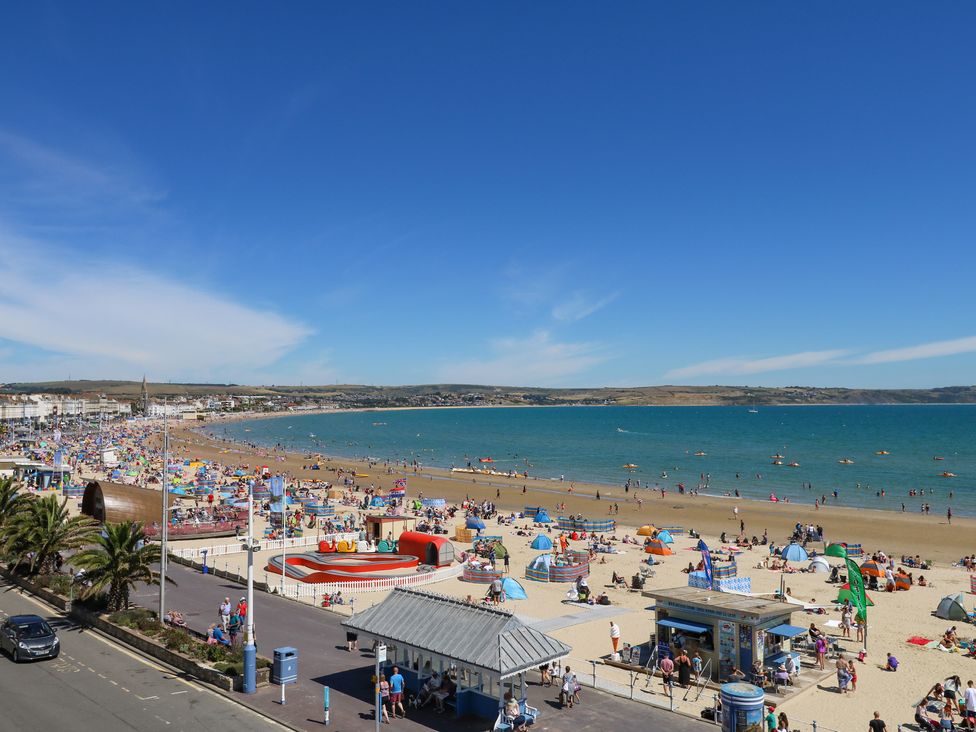 A crowded sandy beach with people sunbathing and swimming near a promenade with palm trees and buildings by the sea at Seaside House in Weymouth