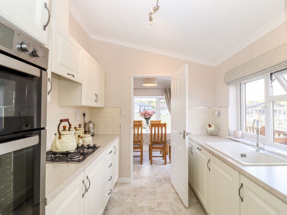 A kitchen with white cabinets a built in oven a stove a sink and a view through a door into a dining area at 12 Bucklesham Park in Bucklesham near Trimley St Martin
