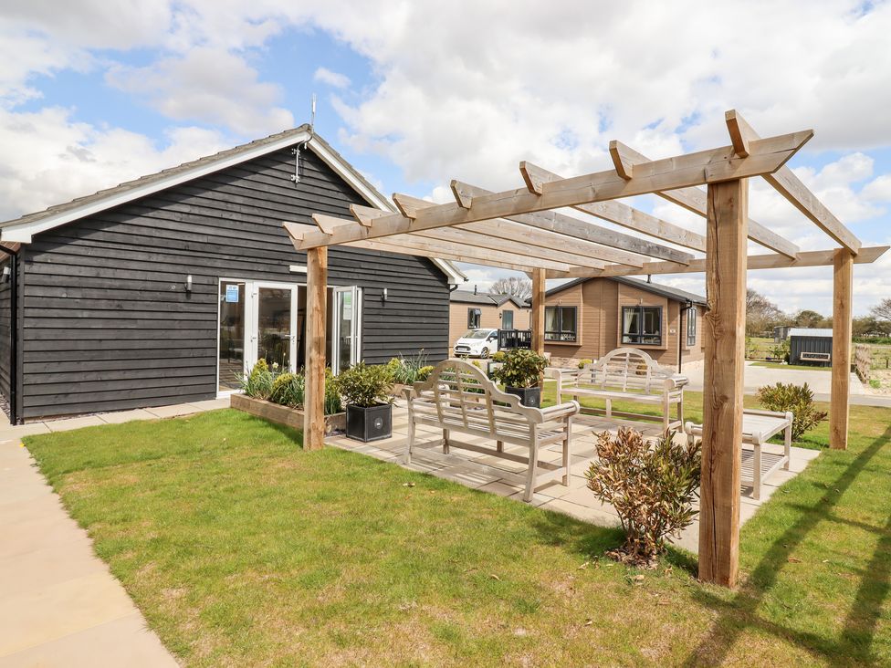 An outdoor seating area with benches under a wooden pergola next to a black building at 12 Bucklesham Park in Bucklesham near Trimley St Martin