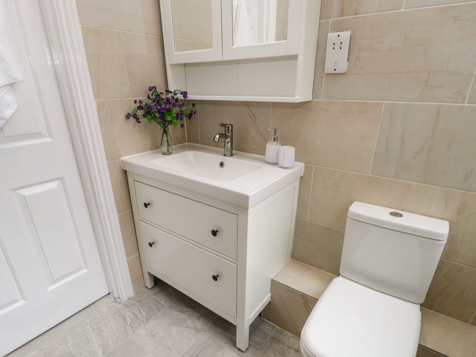 A bathroom with a white sink cabinet with a faucet and flowers on the counter next to a white toilet at Flat 3 in Loftus