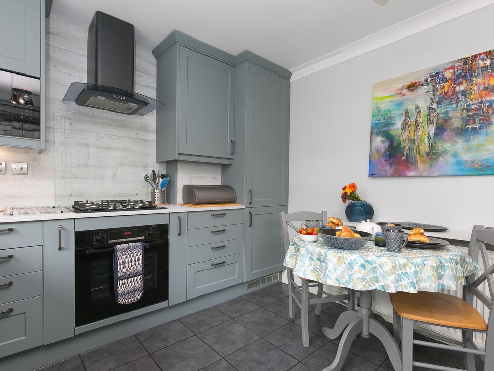 A kitchen with grey cabinets a gas stove an oven and a dining table set with food and a colorful painting on the wall at Huers Hide in Carbis Bay