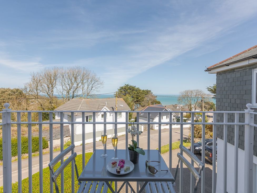 A balcony with a table and chairs overlooking houses and the sea at Kerensa in Carbis Bay