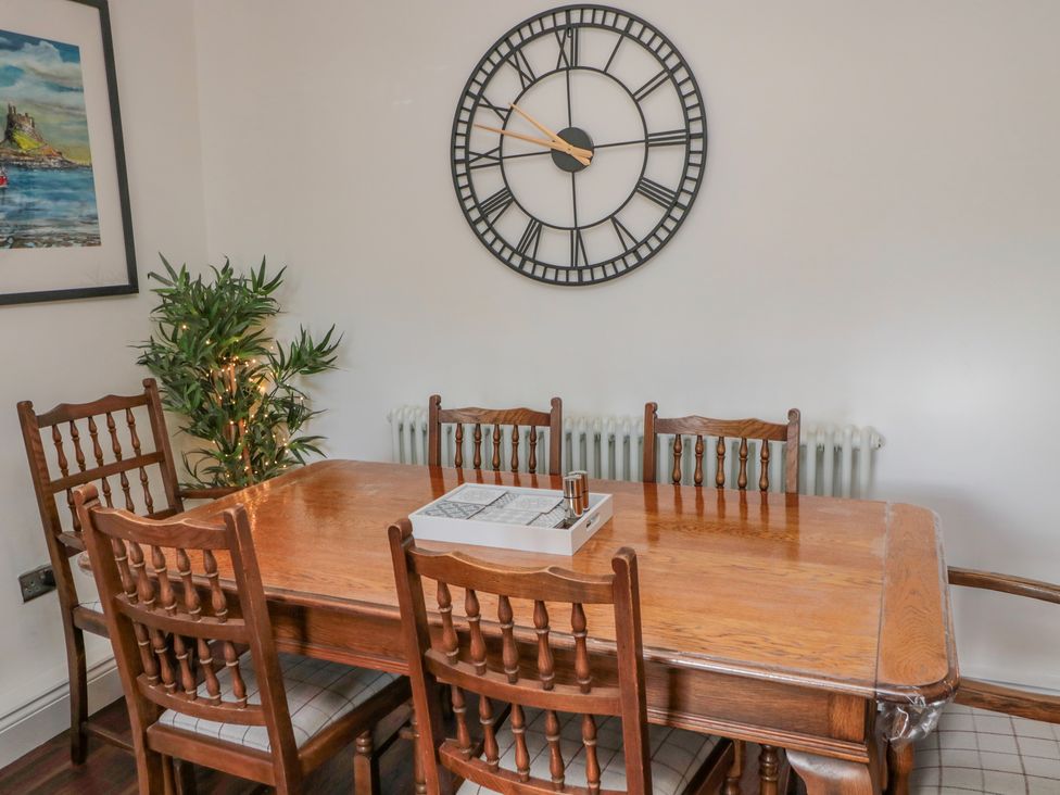 A dining room with a wooden table and six wooden chairs a large wall clock and a framed picture at Woolley Lodge in Wooler