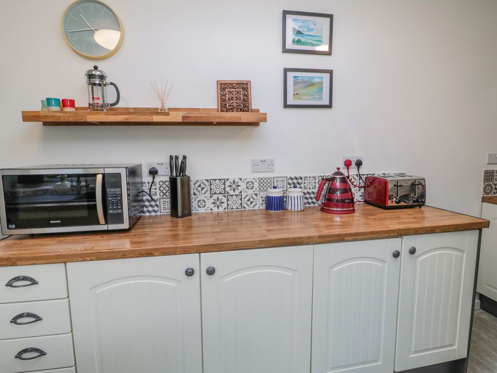 A kitchen counter with microwave knives kettle toaster and cups with a wall clock and framed pictures above at Woolley Lodge in Wooler