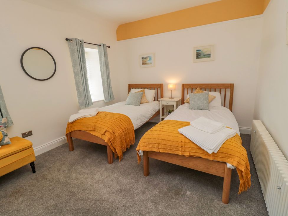 A bedroom with two single beds with orange throws and a nightstand with a lamp at Woolley Lodge in Wooler