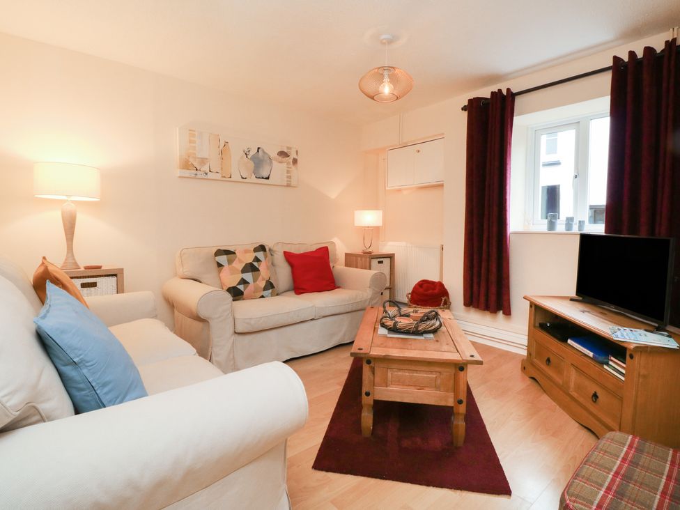 A living room with cream sofas cushions a wooden coffee table a TV on a wooden stand and dark red curtains at Courtyard Cottage in Chittlehampton
