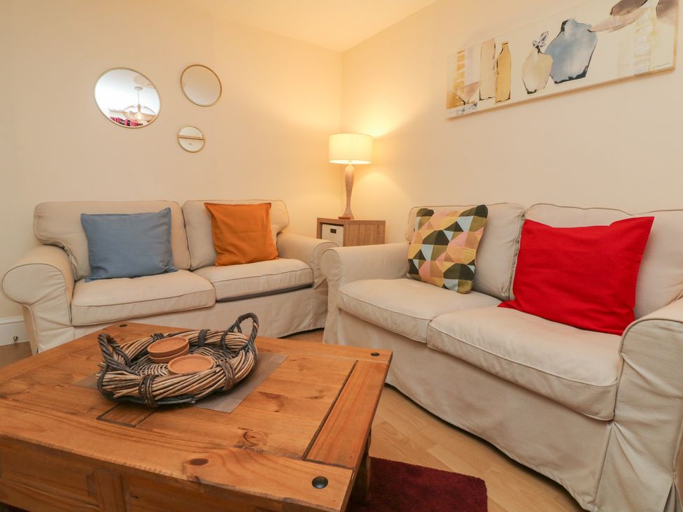 A living room with two beige sofas with colorful cushions a wooden coffee table a lamp on a side table and three round mirrors on the wall at Courtyard Cottage in Chittlehampton