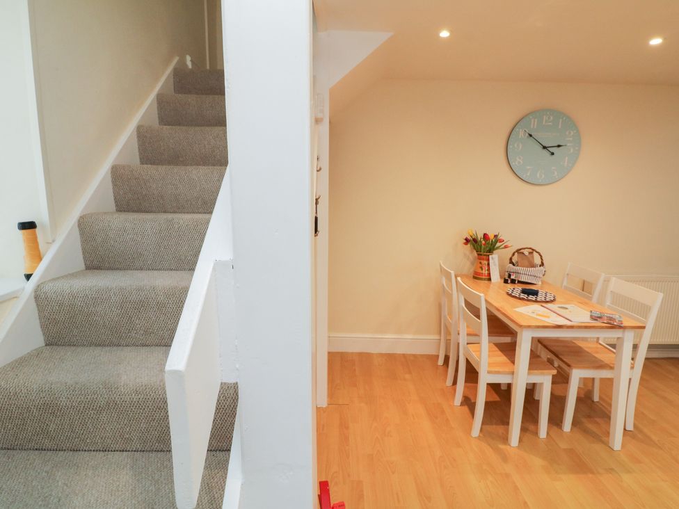 A dining area with a wooden table and chairs next to carpeted stairs at Courtyard Cottage in Chittlehampton