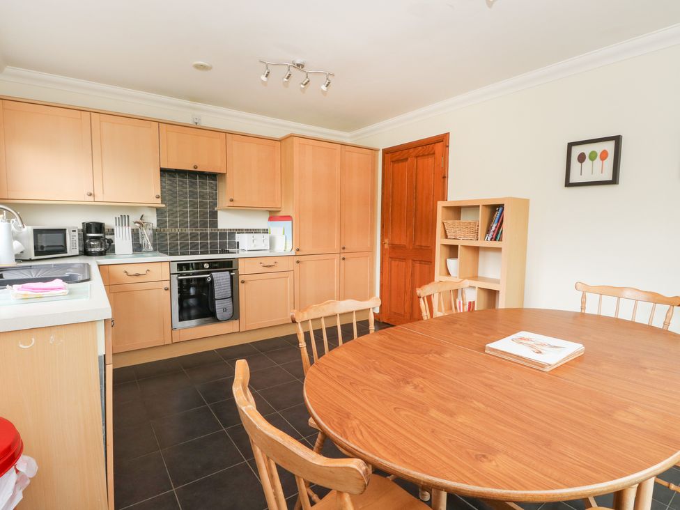 A kitchen with wooden cabinets a round dining table with chairs and a bookshelf at Brae Mhor Cottage in Fort William