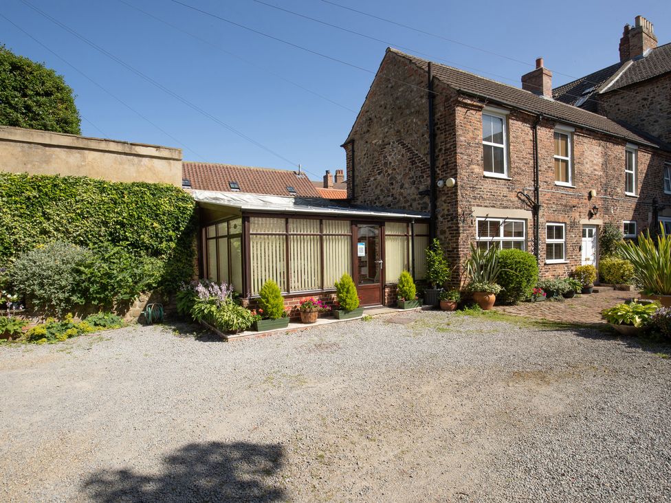 An exterior view of a stone house with a gravel driveway and a glass porch surrounded by potted plants at The Georgian Cottage in Bedale