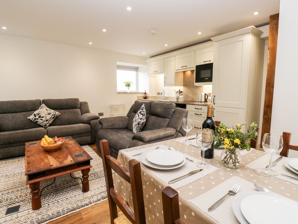 A dining table with plates and wine glasses next to a living area with sofas and a wooden coffee table in an open kitchen space at 2 Barn Cottages in Norwood Green