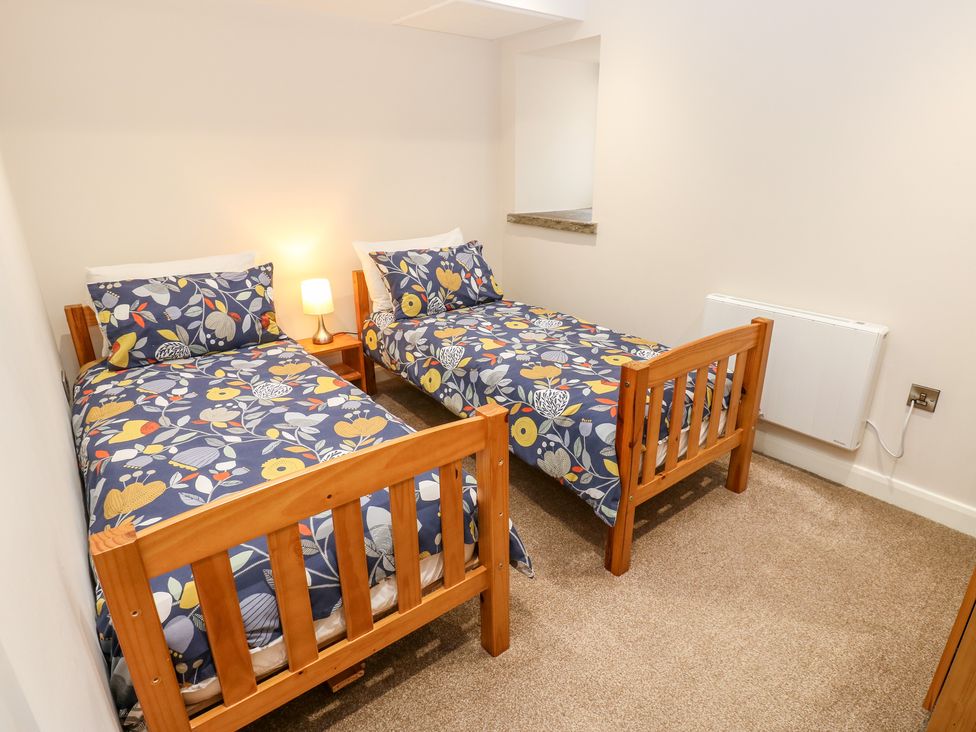 A bedroom with two wooden single beds with floral bedding and a small wooden nightstand with a lamp at 2 Barn Cottages in Norwood Green