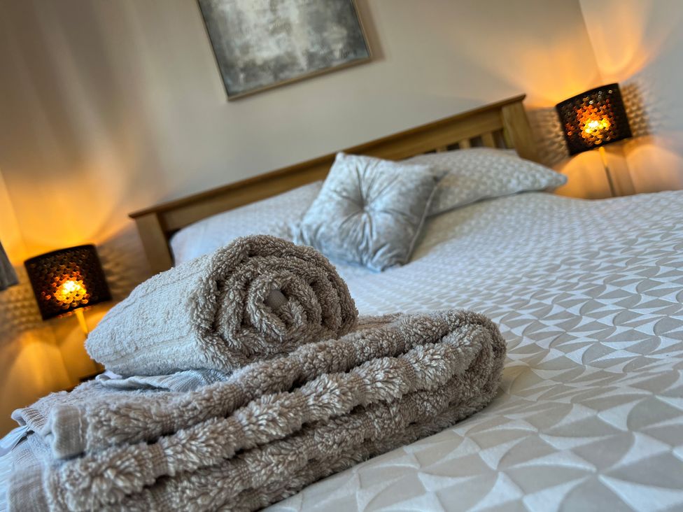 A bedroom with a wooden bed a patterned bedspread two folded towels and two bedside lamps at Gone Crabbing in The Bay Filey