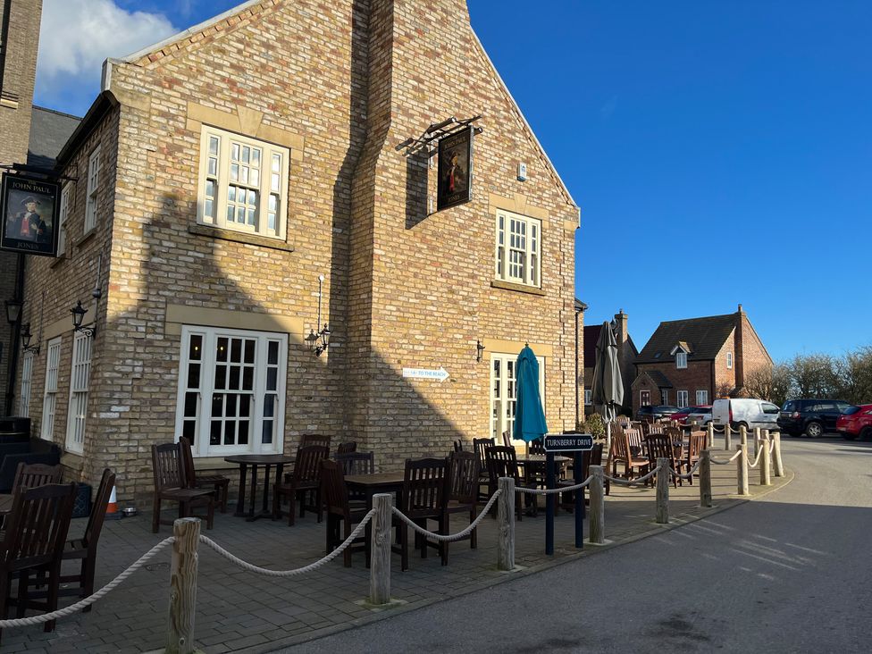 An outdoor seating area with wooden chairs and tables outside a brick building with multiple windows on Turnberry Drive