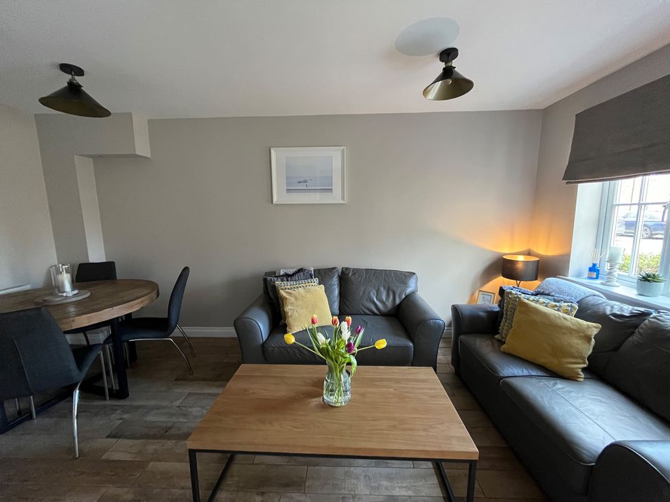 A living room with two leather sofas yellow cushions a wooden coffee table with flowers and a round dining table with chairs at Gone Crabbing in The Bay Filey