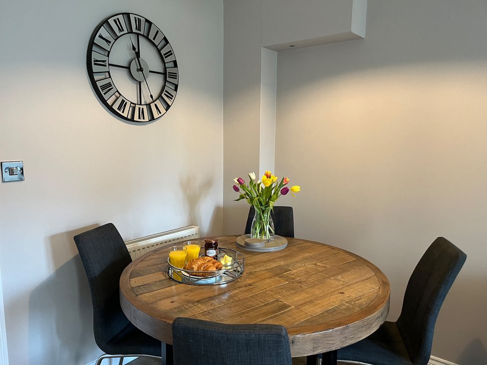 A wooden round dining table with four dark chairs and a vase with tulips on the table at Gone Crabbing in The Bay Filey